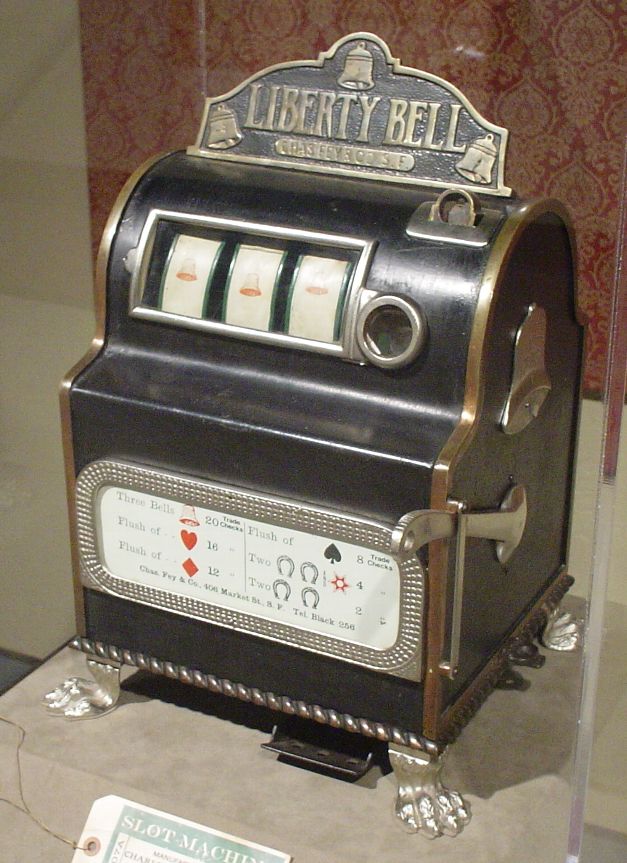 Charles Fey’s original cast-iron Liberty Bell slot machine in a museum case — three reels, claw feet, and a payout table crediting Chas. Fey & Co., 406 Market St., S.F.